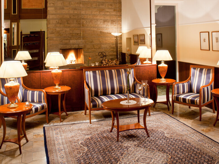 In einem Raum stehen alte Sessel um einen kleinen Kaffeetisch herum während das Zimmer von antiken Lampen beleuchtet wird.