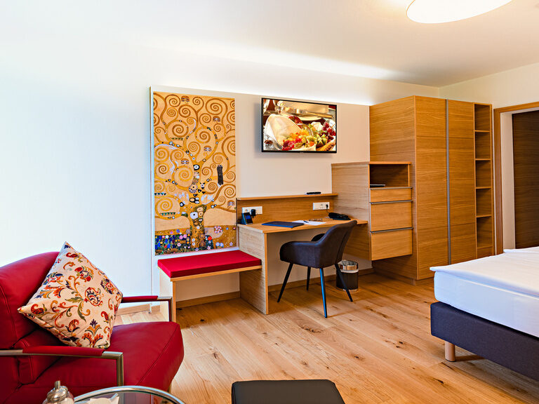 Das Design des Doppelzimmers Komfort überzeugt mit seinen roten Sesseln und seinem hölzernen Schreibtisch