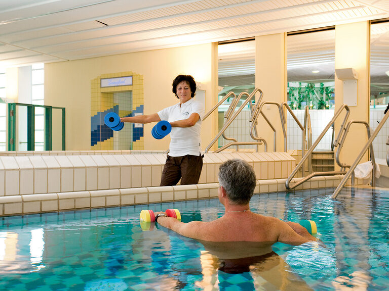 Ein Mann in einem Becken in der Rottal Terme führt Medical Wellness Übungen mit einer Trainerin aus.