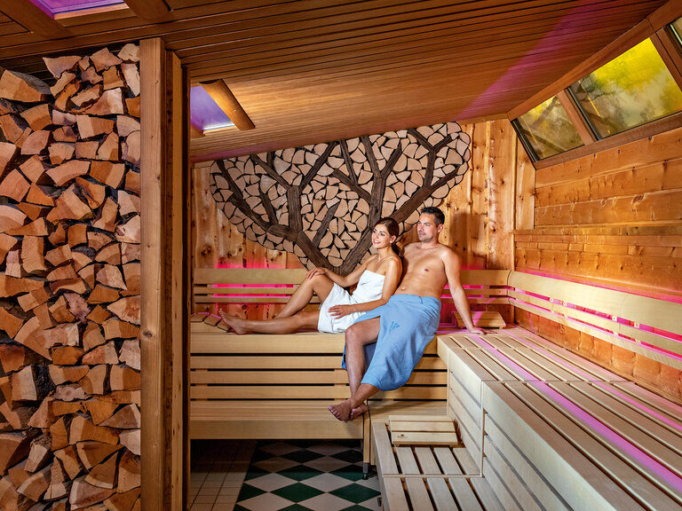 Ein paar sitzt auf einer hölzernen Bank in der Zirbelsauna